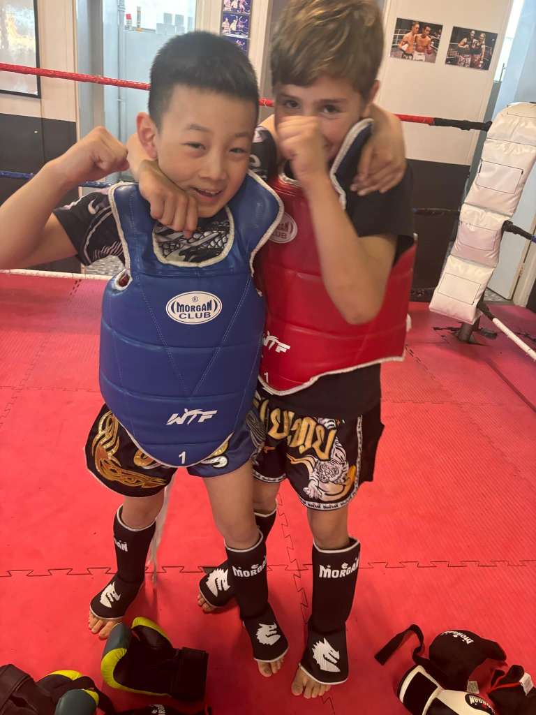 kids class, Kids practicing Thai boxing in a fun and energetic class, wearing gloves and focusing on their techniques with a coach guiding them.